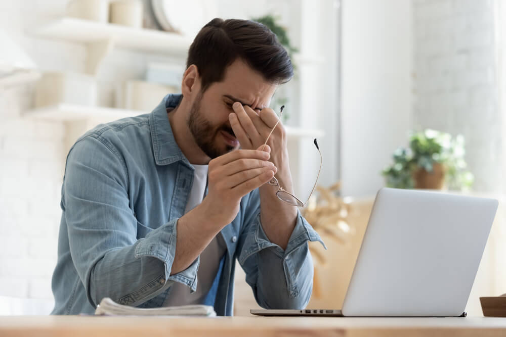 Tired young man feel pain eyestrain holding glasses rubbing dry irritated eyes fatigued from computer work